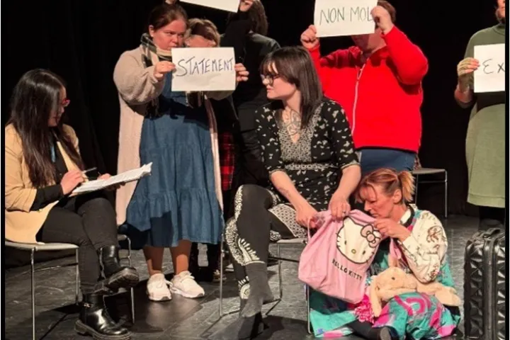 Group of women on stage performing a play on domestic abuse prevention with placards of words "Statement" "Occupation" "NON-MOL" 