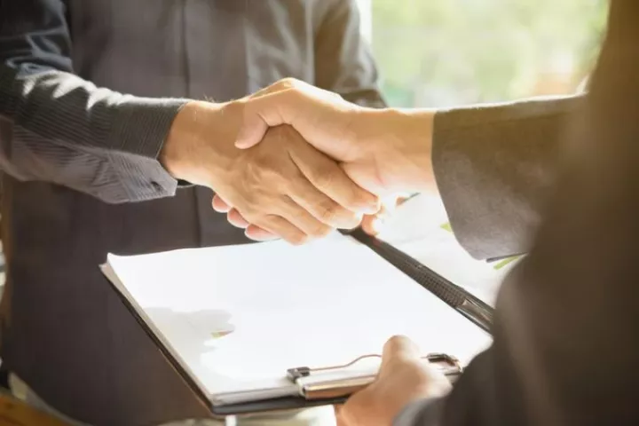 Two people shaking hands above a clipboard with a contract