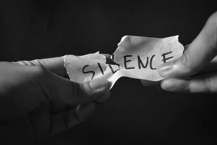Word "Silence" written on paper and torn in half with two hands holding each end
