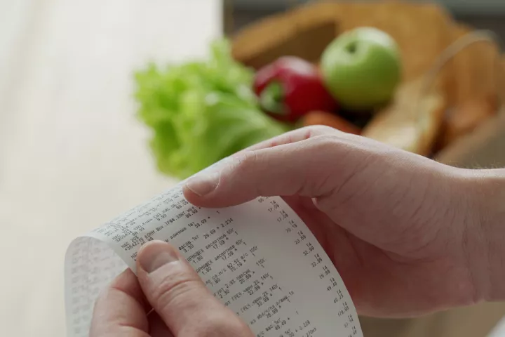 person hold a receipt, there is food in the background