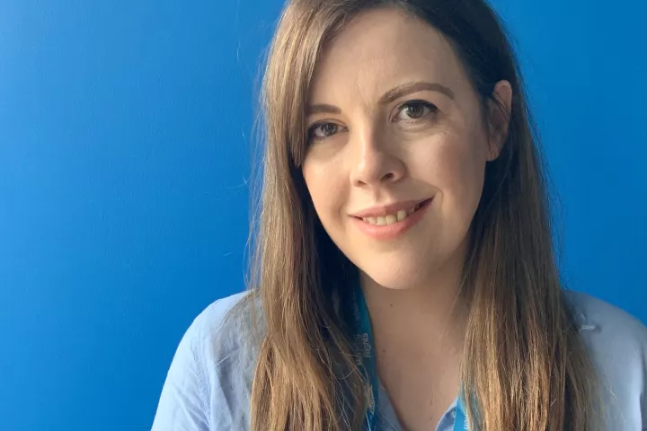 Kate McCauley, Housing Rights CEO standing in front of a blue background smiling