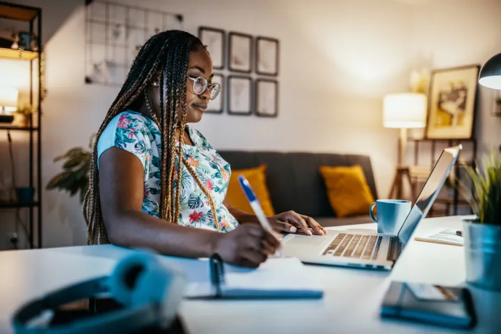 Woman taking notes and looking at a laptop