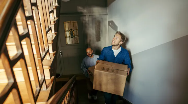 Man climbing upstairs carrying boxes of household items
